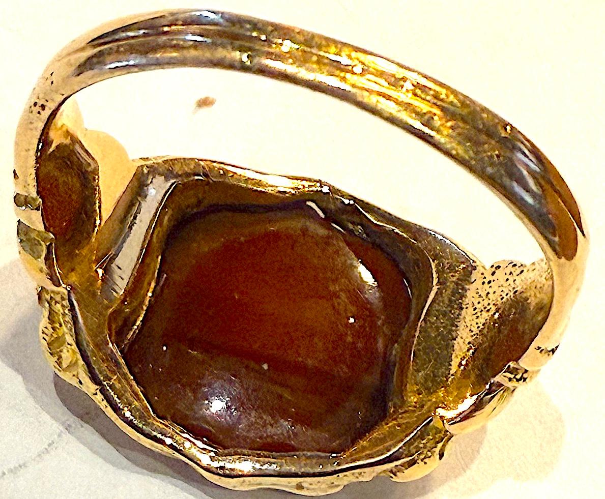 Bague héraldique ancienne de forme inhabituelle en forme de bouclier, sertie d'une agate de cornaline bicolore. Les épaules sont ornées d'un motif repoussé en relief, digne d'une bague destinée à contenir un blason familial.

Cette bague n'est
