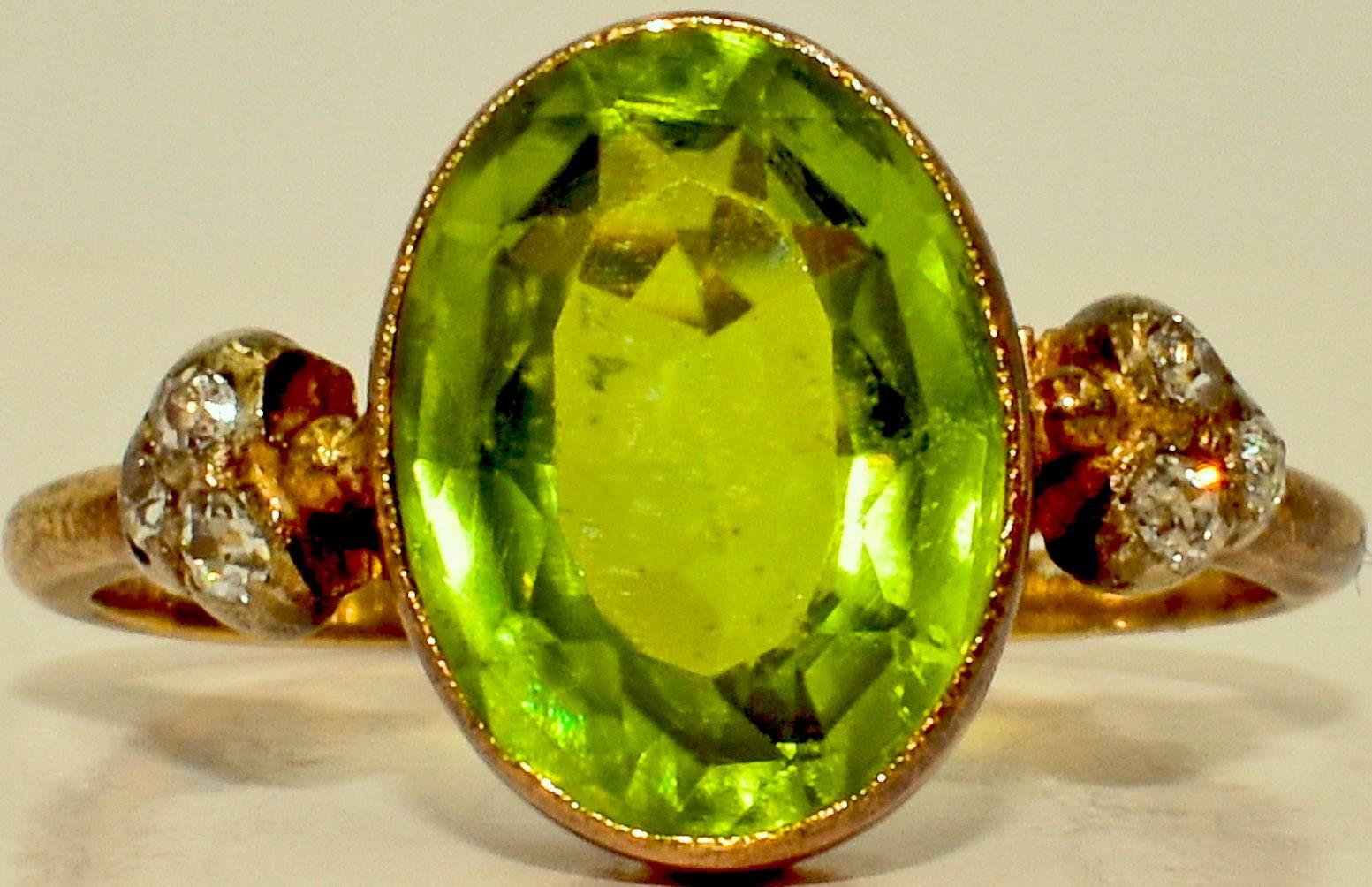 Colorful Victorian peridot ring. The beautiful green stone is flanked by a cluster of three diamonds on each side. The stones are set in 18K gold.  The ring is a size 5 1/5 and can easily made larger. Peridot is a well-known and ancient gemstone,