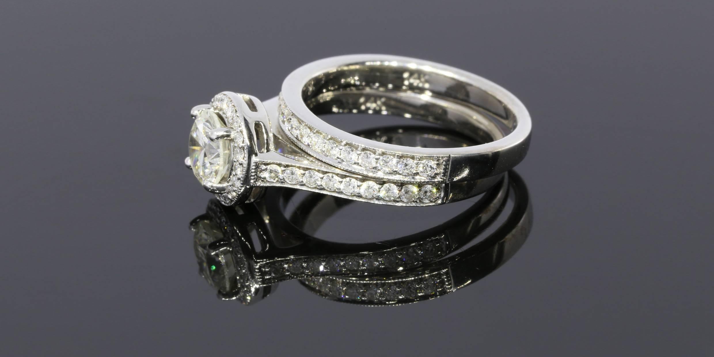 This beautiful bridal set has a total weight of 1.18 carats and features a gorgeous halo engagement ring and matching wedding band. Both are set in 14 karat white gold with milgrain edges and a bright finish.

The engagement ring has a fiery, .73