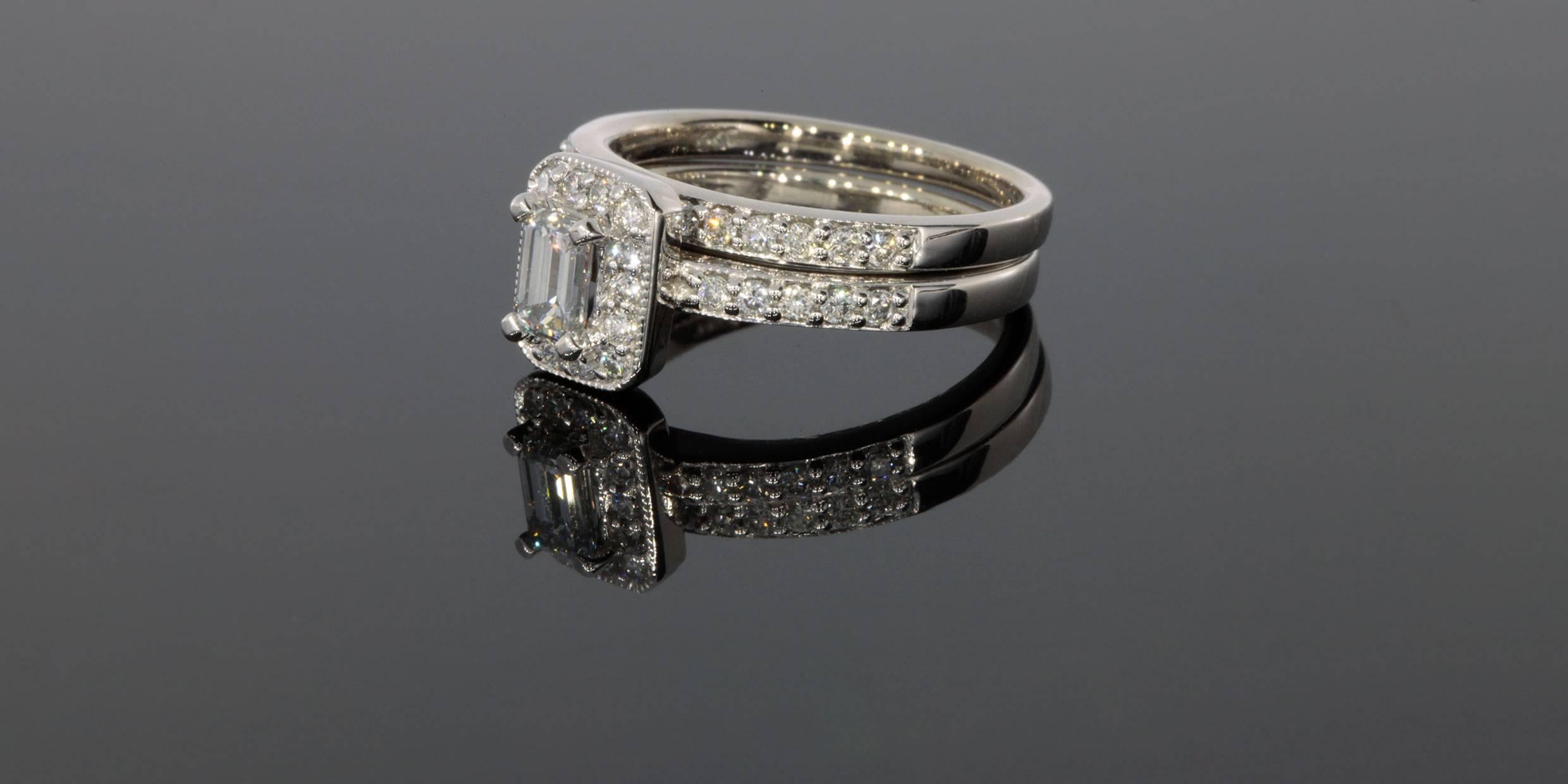 This classic engagement ring features a beautiful .47 carat emerald cut diamond center stone that grades as I/SI2 in quality. This diamond is prong set in a halo diamond engagement ring with a matching diamond wedding band & both have slight