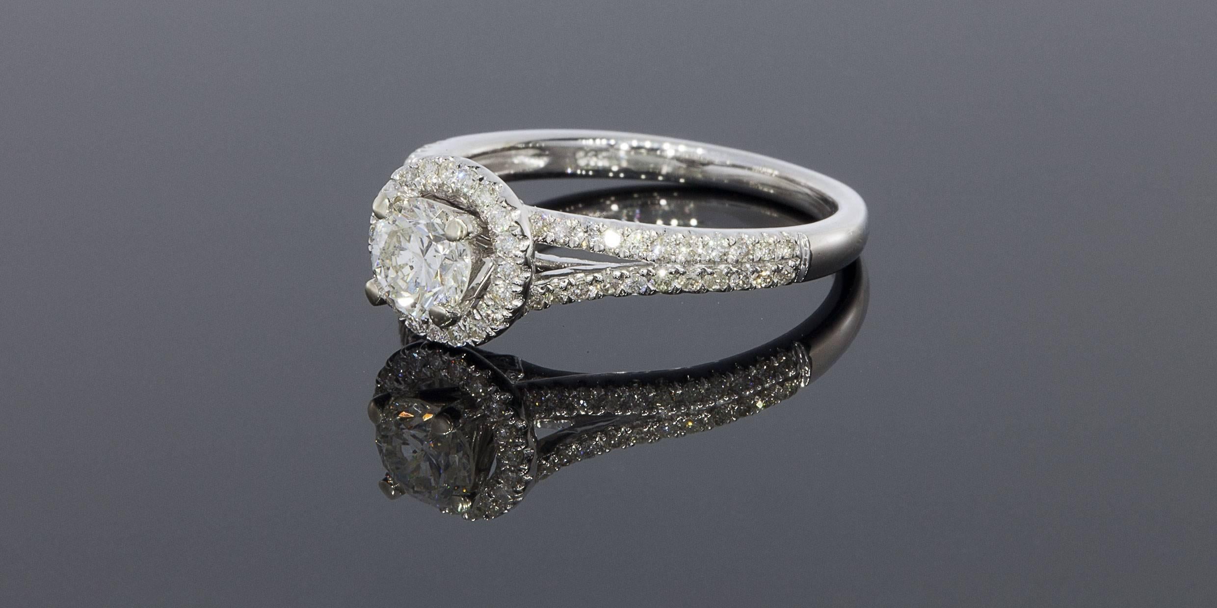 This gorgeous ring sparkles beautifully. It features a .56 carat round brilliant diamond center that grades as J/SI2 in quality according to GIA standards. This glittering center diamond is surrounded by a beautiful pave set halo of diamonds. The