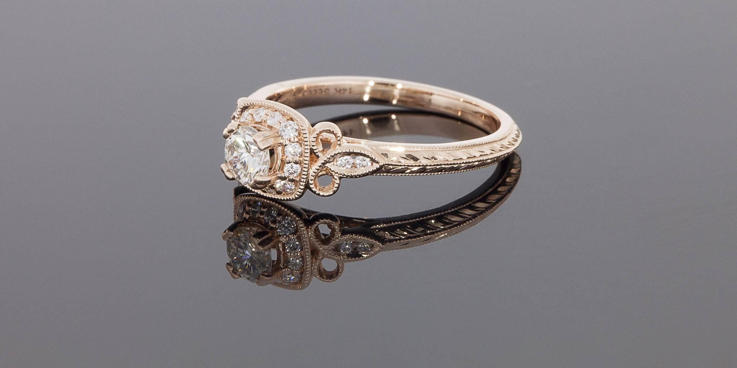 This beautiful rose gold engagement ring has lovely, intricate details all over. The center diamond is a .30 carat round brilliant cut that is J/VS2 in quality. It is split prong set & surrounded by a cushion shaped, milgrain accented halo of bead