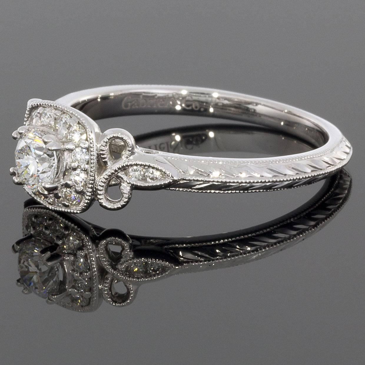 This vintage-inspired engagement ring is pure romance. A .35ctw diamond halo framed by floral-inspired accents embraces the .23ct round cut center diamond. Milgrain details embellish the 14k white gold knife edge band.

Details:
14K White