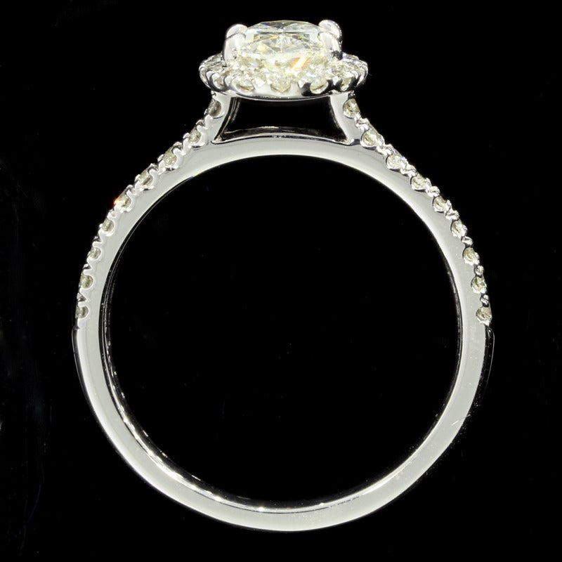 The ring features one oval brilliant cut center diamond weighing 0.83CT. The diamond is K/VS2 in quality. The diamond is set in a four prong halo. The ring also features round brilliant cut diamonds weighing 0.40CTW. The diamonds are G/SI1 in