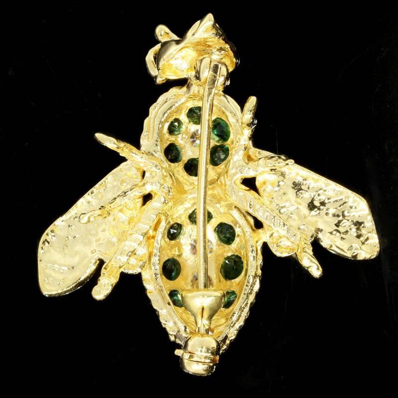 This fun & beautiful yellow gold pin/brooch features 5 round brilliant cut diamonds and 13 round brilliant cut emeralds with a total carat weight of 0.90 carats. The pin is comprised of 14 karat yellow gold & measures approximately 1 inch by 1 inch