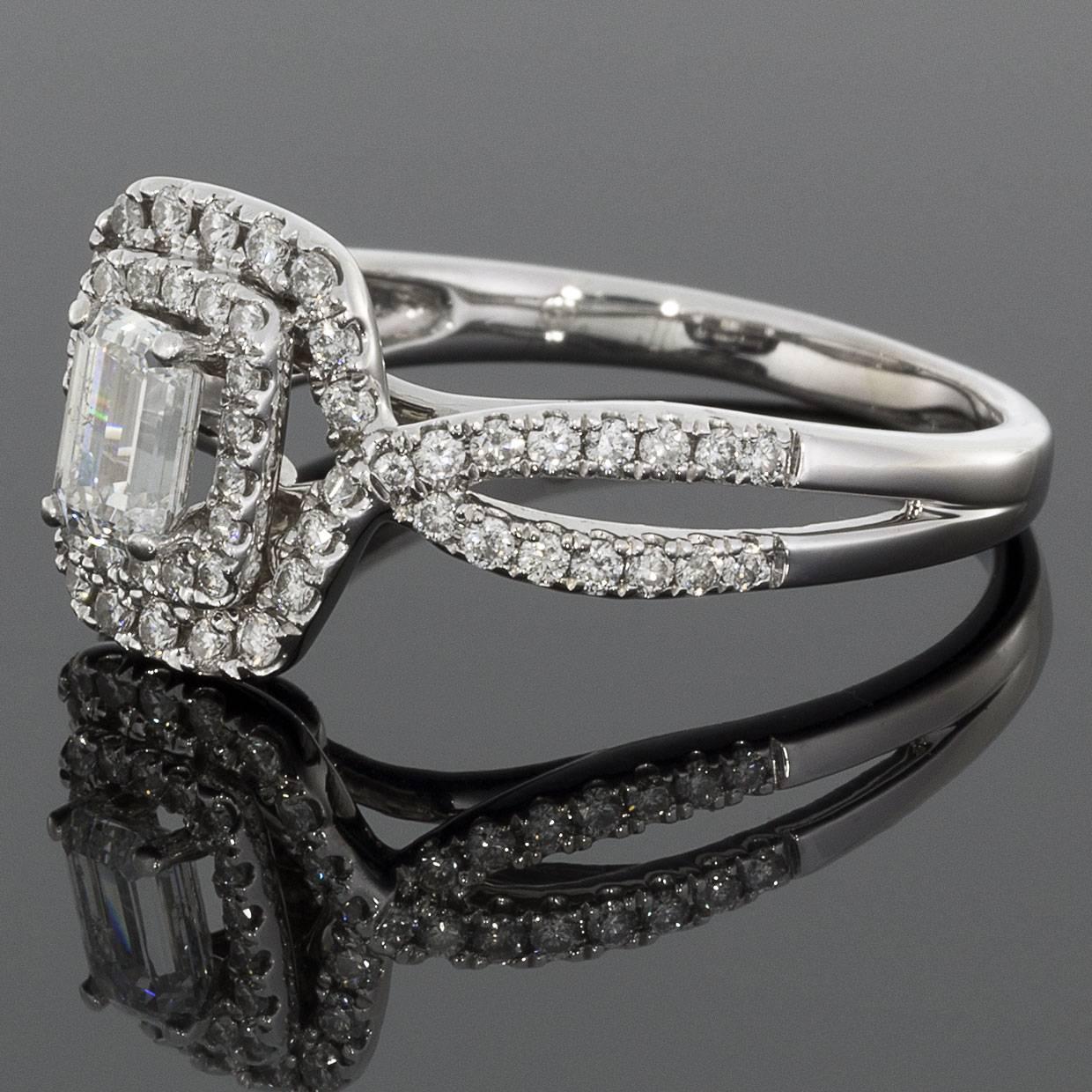 This gorgeous halo engagement ring has a big look with its lovely double halo flowing gracefully from the twisted, split shank. The center diamond is a 1/2 carat emerald cut diamond that grades as H/SI1 in quality. It is prong set in the center of