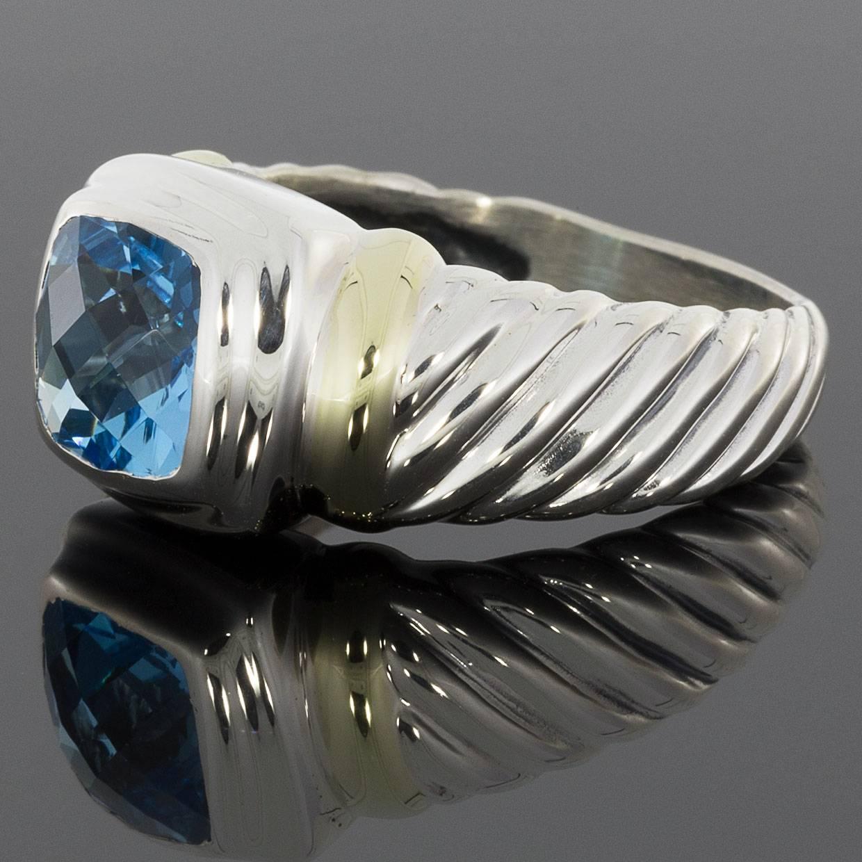 This beautiful David Yurman ring is from the Noblesse Collection. It features a square cushion cut blue topaz that is bezel set. The ring is comprised of sterling silver with 14 karat yellow gold accents. The shank features Yurman's signature cable