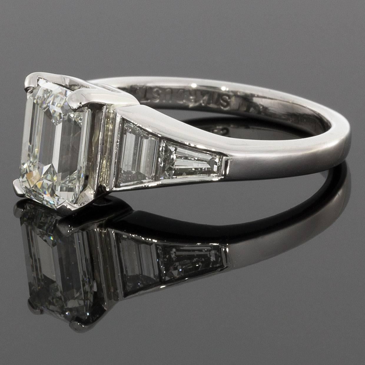 This spectacular ring features a gorgeous Art Deco style design. The dazzling center diamond is a 1.53 carat emerald cut diamond that is GIA certified as I/VS2 in quality. It is prong set in a vintage platinum ring. The ring also features beautiful,