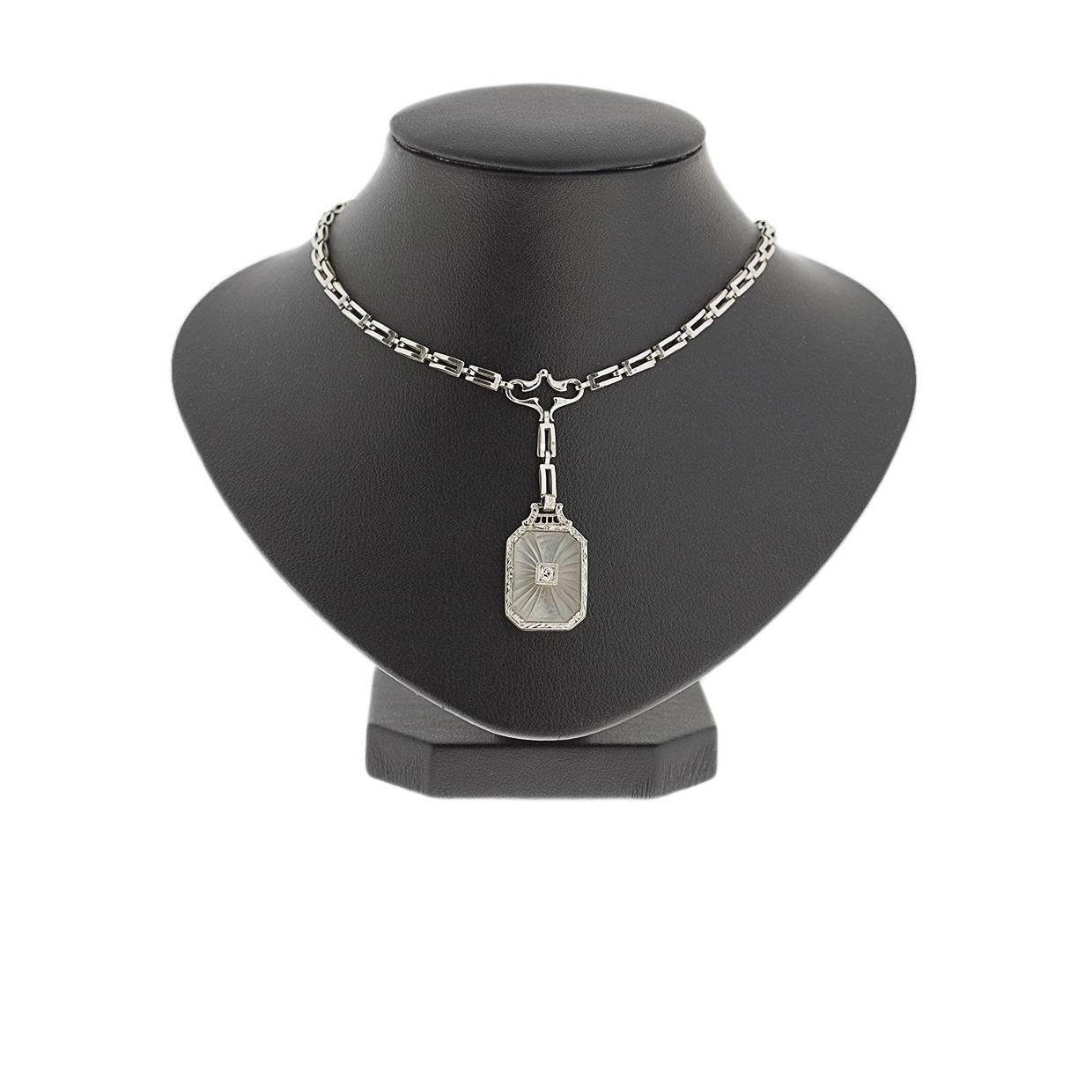 This beautiful estate necklace features a unique vintage design. The center pendant features a carved, frosted crystal with a single small diamond at its center. This crystal is bezel set in 14 karat white gold with a very intricately engraved