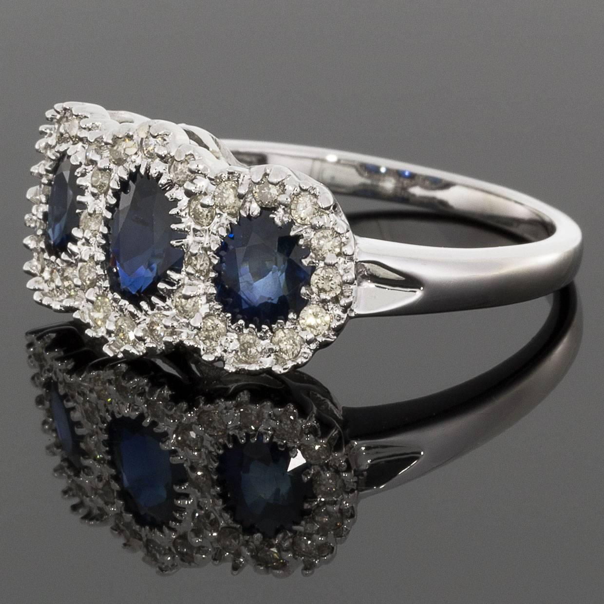 This elegant ring features 3 beautiful, natural, oval cut, blue sapphire center stones. These luscious sapphires are multi prong set in a 14 karat white gold ring, & they are surrounded by a halos of round brilliant diamonds. Captivating with