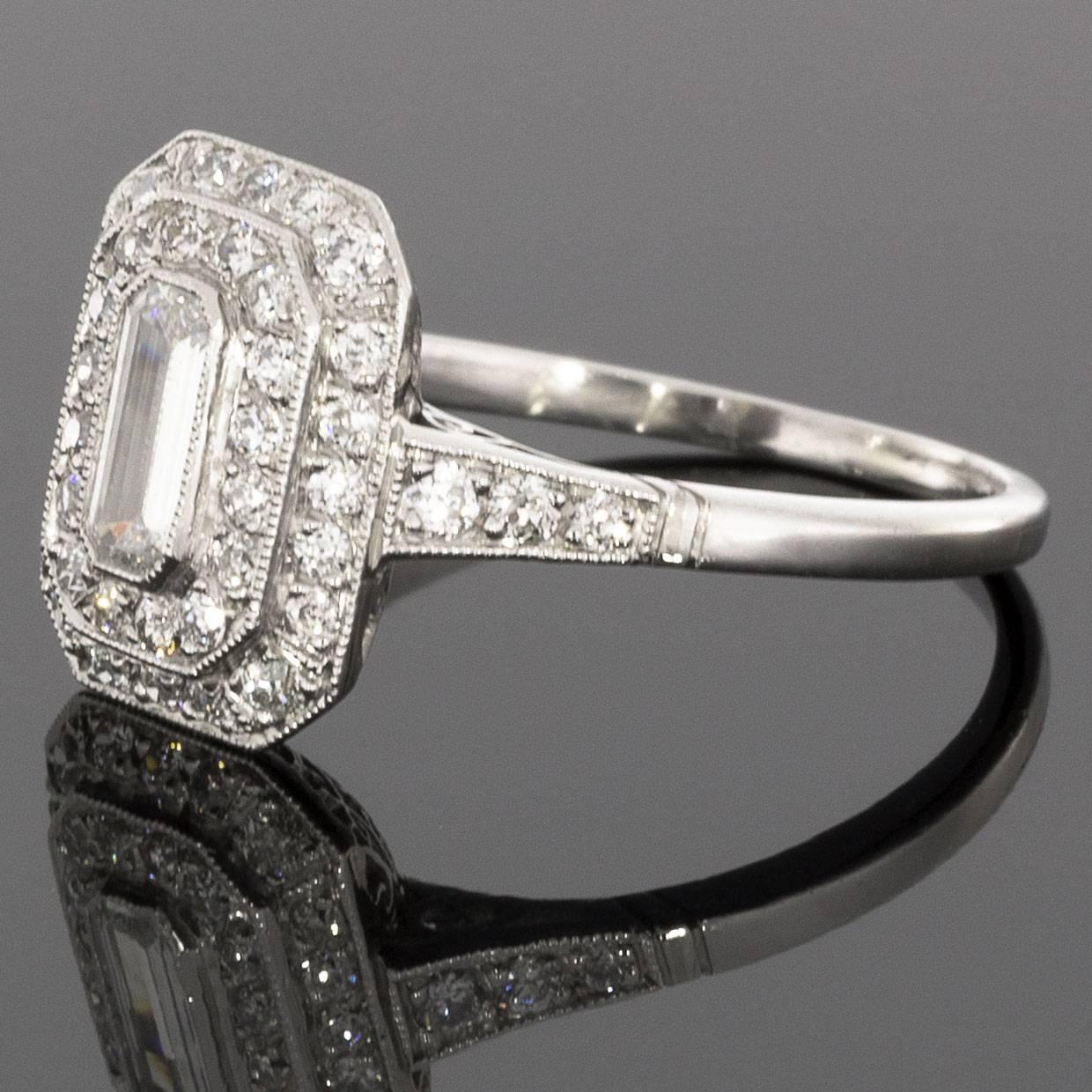 This gorgeous halo engagement ring has a big look with its lovely double halo flowing gracefully from the petite, diamond shoulder shank. The center diamond is a .70 carat emerald cut diamond that grades as I/SI1 in quality. It is bezel set in the