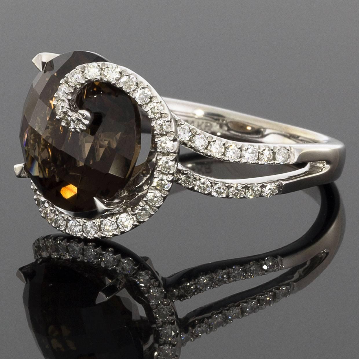 This stunning ring features an 11 mm, round, checkerboard faceted smokey quartz gemstone center. Radiant & warm with its beautiful shades of brown, this smokey quartz is surrounded by graceful diamond swirl. Comprised of 14 karat white gold, the
