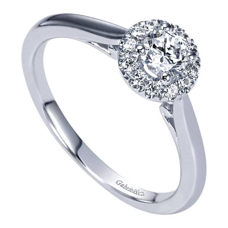This lovely Gabriel & Co engagement ring has a timeless & clean halo design. The ring features a round brilliant cut diamond center that weighs .23 carat & grades as I/SI1 in quality. This glistening diamond is surrounded by a halo of prong set