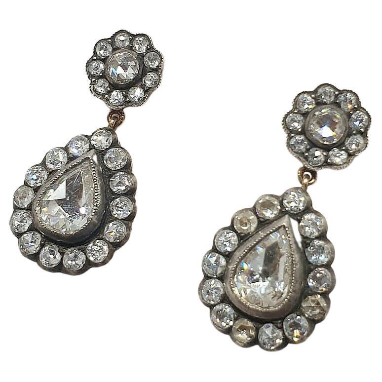 Antique dangling earings centered with 2 pear shape rose cut diamonds with estimate weight of 4 carats diameter 9.17mm×7mm decorted with a diamond flower on top with ceveral smaller rose cut diamonds earrings is 14k gold topped with silver in closed