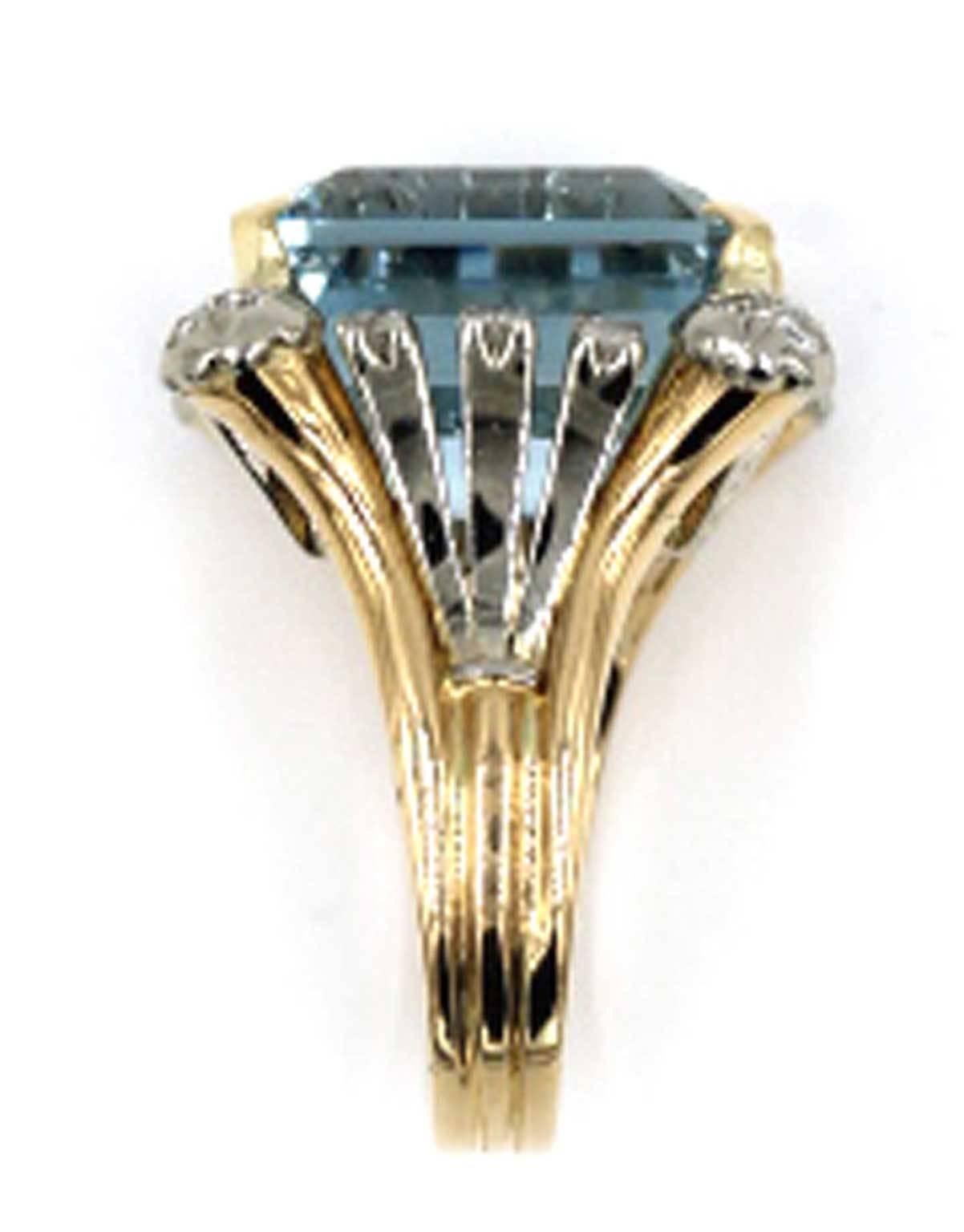 This fabulous vintage ring features a 19-carat Emerald Cut Aquamarine surrounded by 24 single cut diamonds equaling .65 CTTW. The two tone gold is seen on all sides of the ring. The yellow gold in on the outside prongs, and the white gold flourishes