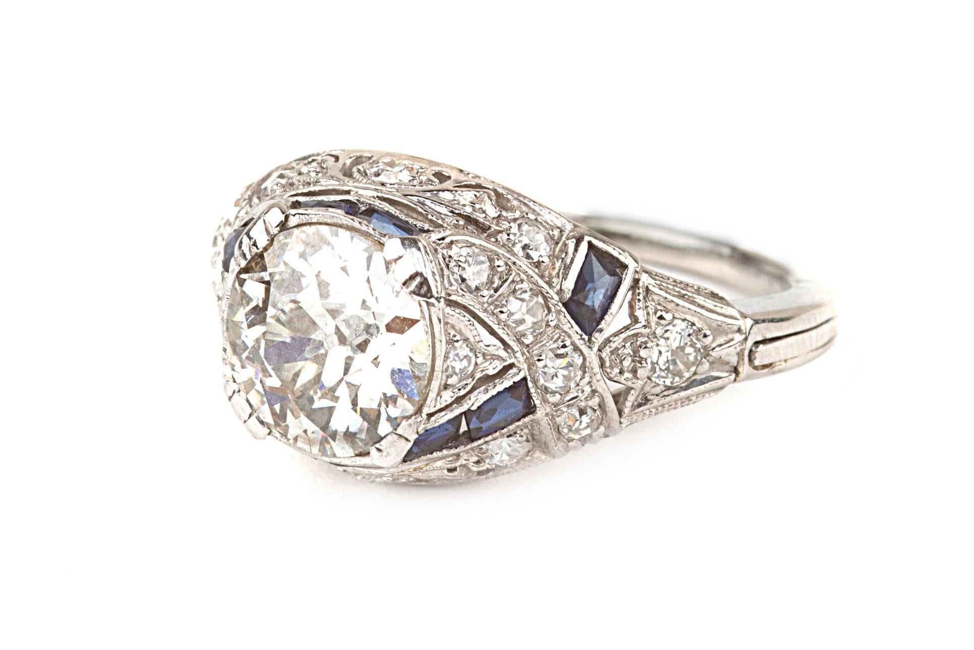 Stunning Art Deco Diamond engagement ring in platinum. The ring features an 1.58 Old European Cut Center Diamond graded I/VS2. There are .37 carats of side diamonds as well as accent sapphires. Total carat diamond weight is approximately 1.95 cttw. 