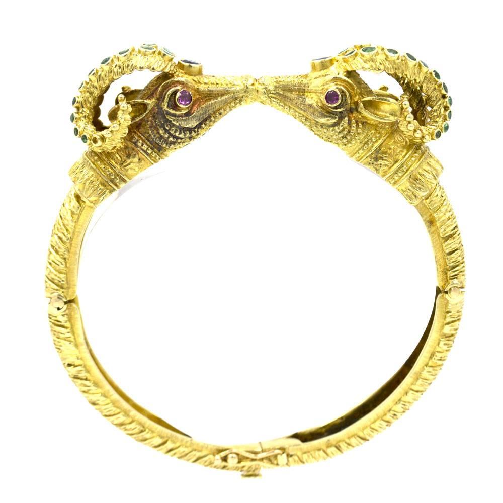 Beautifully crafted bangle bracelet by designer Ilias Lalounis features two kissing ram heads embellished with emeralds, sapphires, and rubies. The Ram's Head in greek methology is a sign of prosperity.  The bangle is signed Lalaounis and