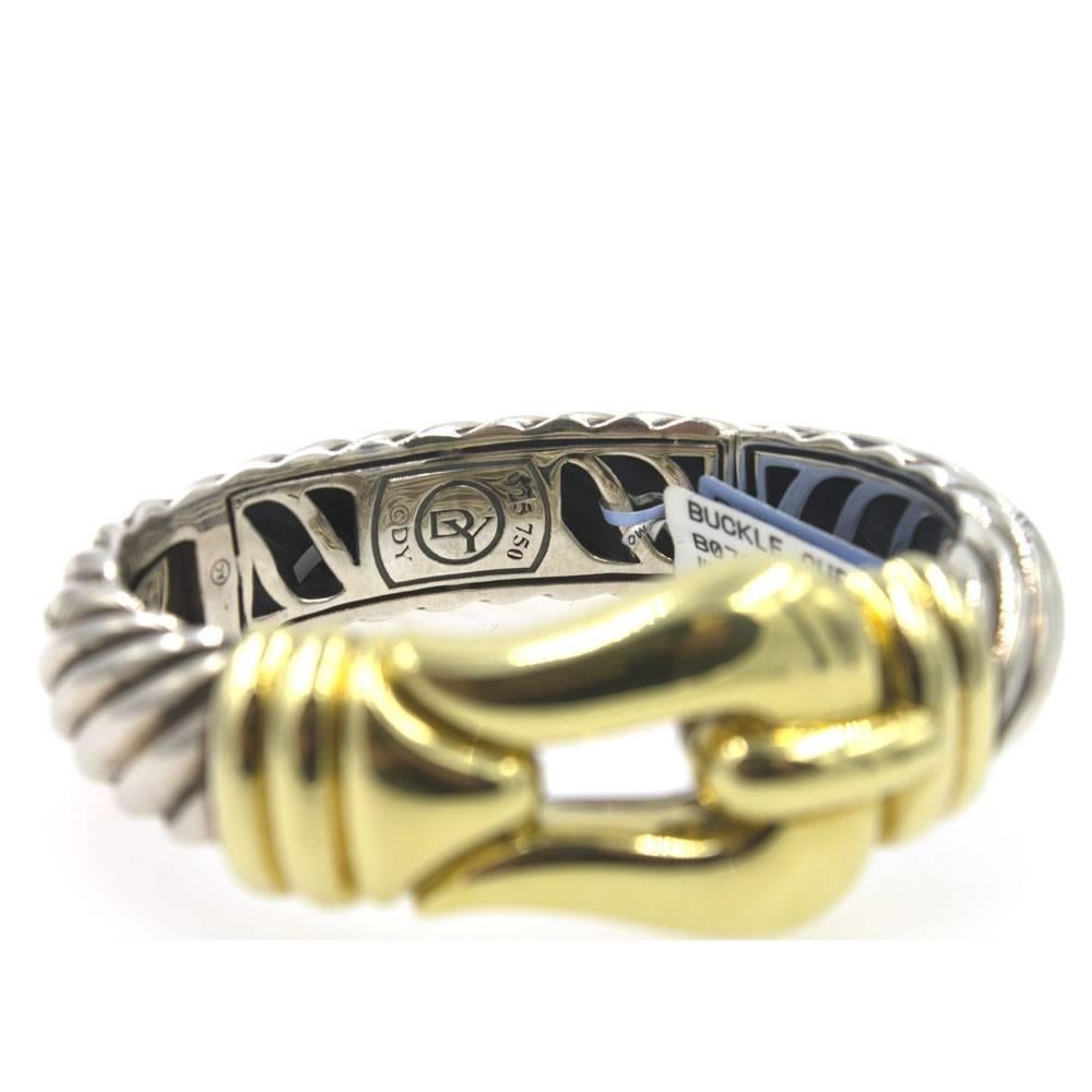 Stylishl David Yurman Two-Tone Cuff Bracelet. The bracelet features an 18 karat yellow gold buckle, and sterling silver cable cuff. The cuff is hinged, and is sized medium measuring 6.5 inches in circumference.  The buckle measures 30mm in width,