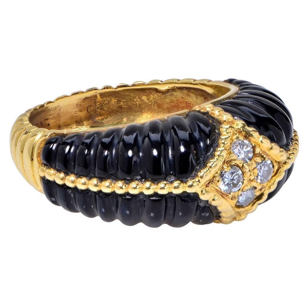This beautiful fashion ring by designer Van Cleef & Arpels features scalloped onyx gemstone and contrasting round brilliant cut diamonds set in 18 karat yellow gold. The four diamonds equal approximately .20 cttw. The ring is signed VCA, numbered