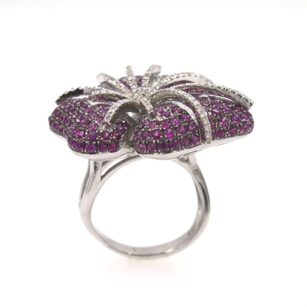 This fabulous vintage fashion ring features rubies and diamonds ( approximately 1.10 carat total weight of diamonds) in the design of a flower. This colorful ring is fashioned in 14 karat white gold, measures 1.5 inches in diameter, and weighs 20.1