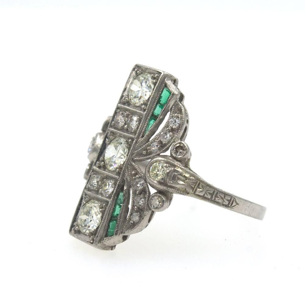 This Magnificant Art Deco Diamond Emerald Ring is Fashioned in Platinum. The cocktail ring features 3 Old European Cut Diamonds that are set in the center from north to south and equal approximately .90 cttw. There are 22 sides diamonds that equal