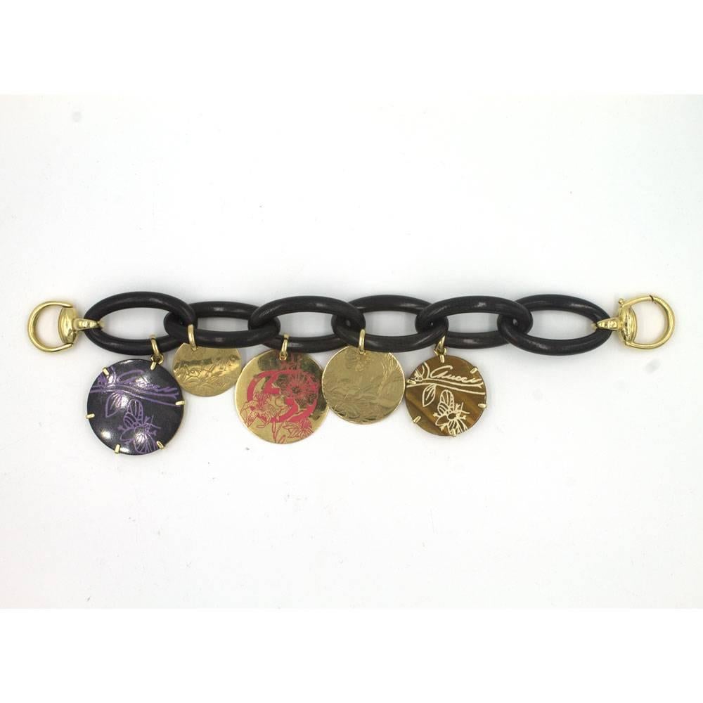 Gucci Flora St. Tropez Charm Fashion Bracelet. This fashionable bracelet features large ebony wood links, 18 karat yellow gold hardware, and 5 Gucci charms. The bracelet features a gold horsebit clasp, and measures 8.5 inches in length. The charms