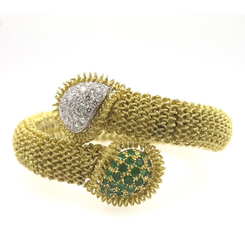 This fabulous bracelet definitely makes a statement. Fashionable and luxurious, this textured 18 karat yellow gold bracelet features emeralds and diamonds in a bypass fashion. One end is set with 2 cttw of diamonds graded H/I color and VS clarity.