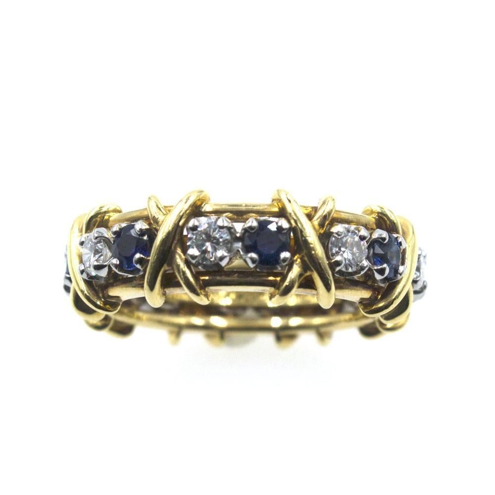 This classic diamond and sapphire 'X' eternity band was designed by Jean Schlumberger for Tiffany & Company. The 18 karat two-tone gold ring features 8 round brilliant cut diamonds alternating with 8 round cut blue sapphires. The ring is size 7, and