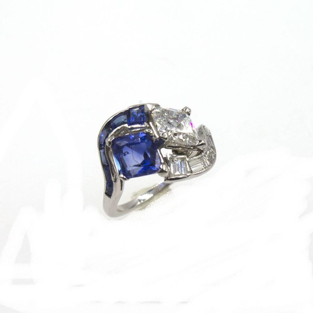This beautiful diamond and sapphire ring from the Late Deco period features a kite shaped diamond and sapphire that sit adjacent to each other with surrounding baguette shaped diamonds and sapphires. The diamond is approximately 1.25 cttw and graded