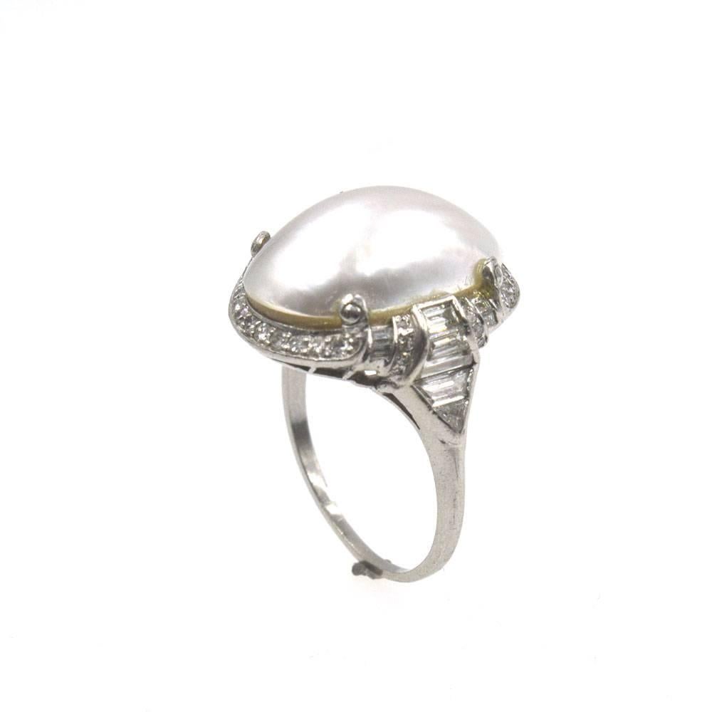 This estate platinum ring features a beautiful deco diamond mounting and mabe pearl center. The mounting features single cut, baguette cut, and trillion cut diamonds that equal approximately 1.00 carat total weight. The top measures 17 x 20mm in