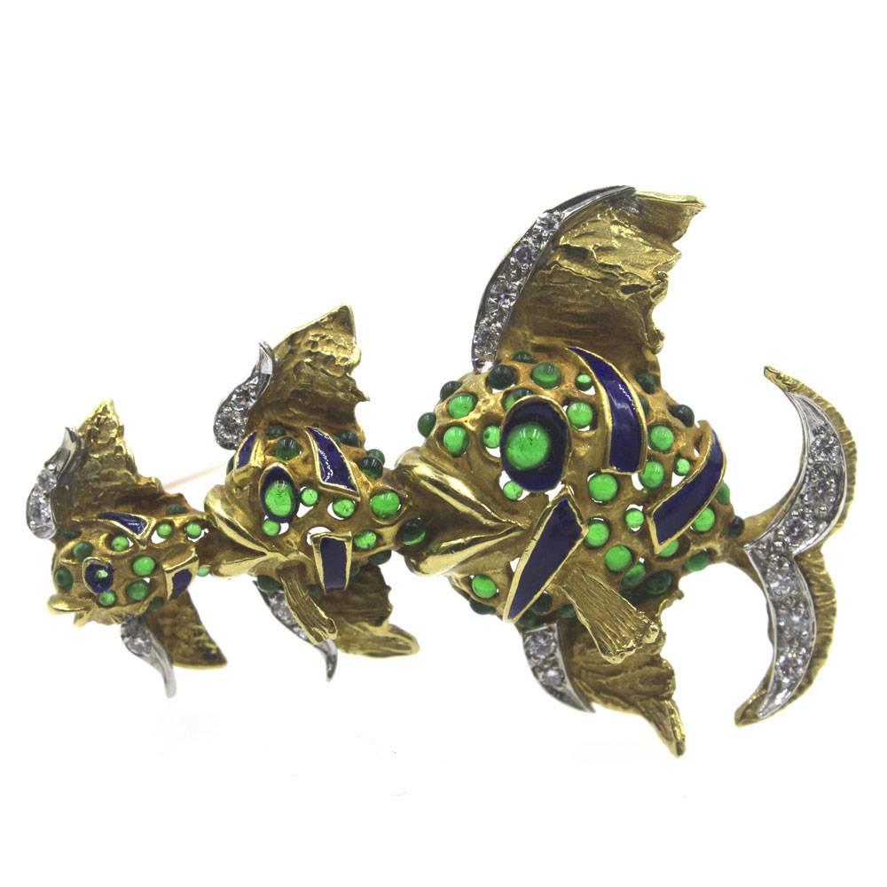 This colorful estate fish pin is crafted in 18 karat yellow gold. The three fish feature colorful enamel, cabochon emerald, and diamond fins. The diamonds equal approximately .30 ctw. The brooch measures 35 x 55mm. 