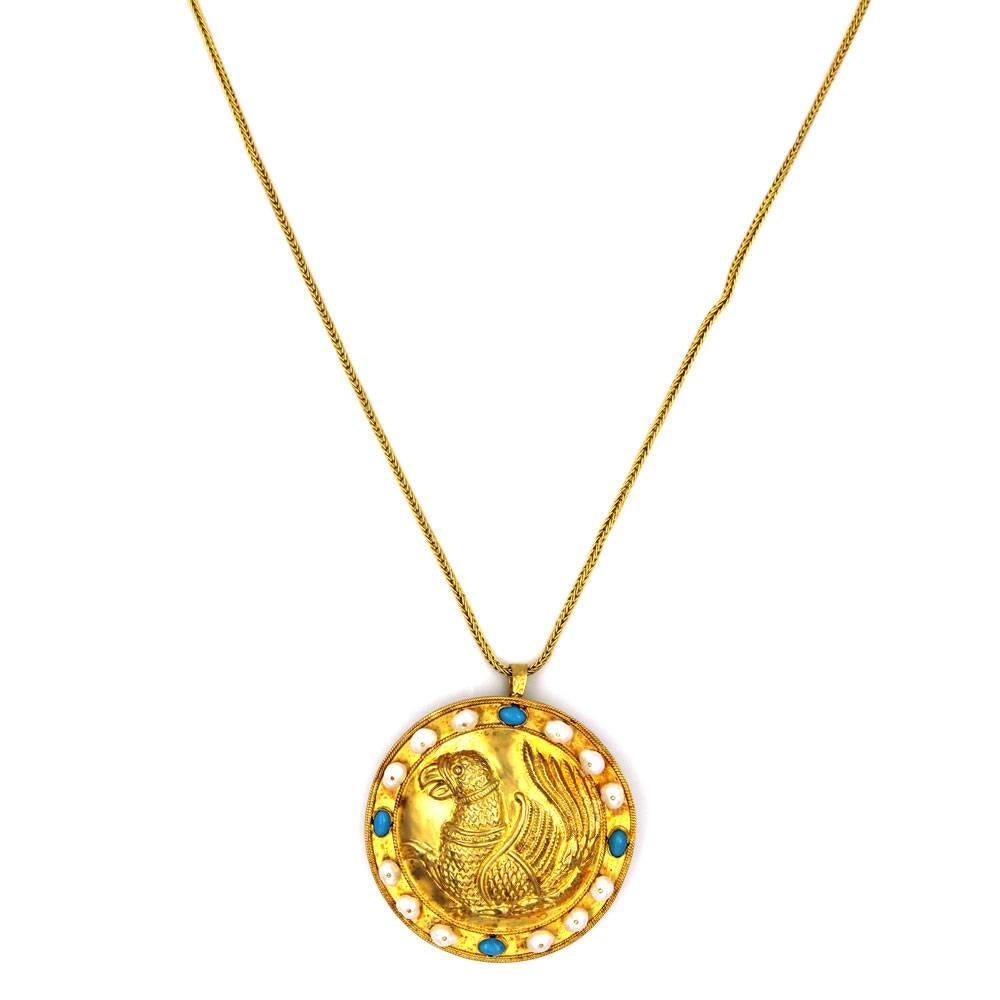 This bold Greek 18 karat yellow gold pendant necklace was designed by Ilias Lalaounis. The pendant/pin features turquoise gemstones, pearls, and a carved methological bird figure. The pendant measures 2.25 inches in diameter, and the necklace is 23
