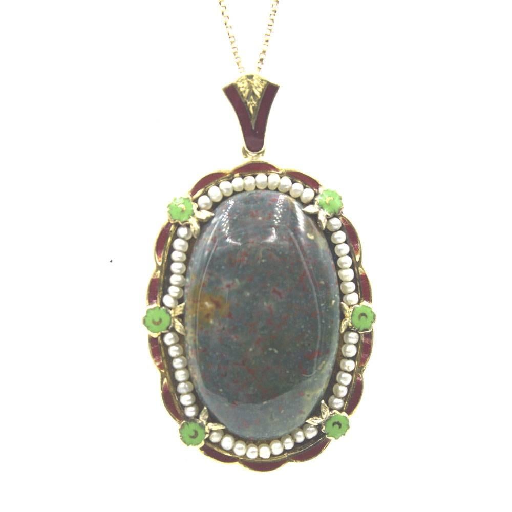 This exquisite antique pendant features a bloodstone gemstone surrounded by an intricate enamel and seed pearl gold frame.  The enamel has been preserved beautifully and is intact. The pendant measures 1 inch in width and 2 inches in height. The 14