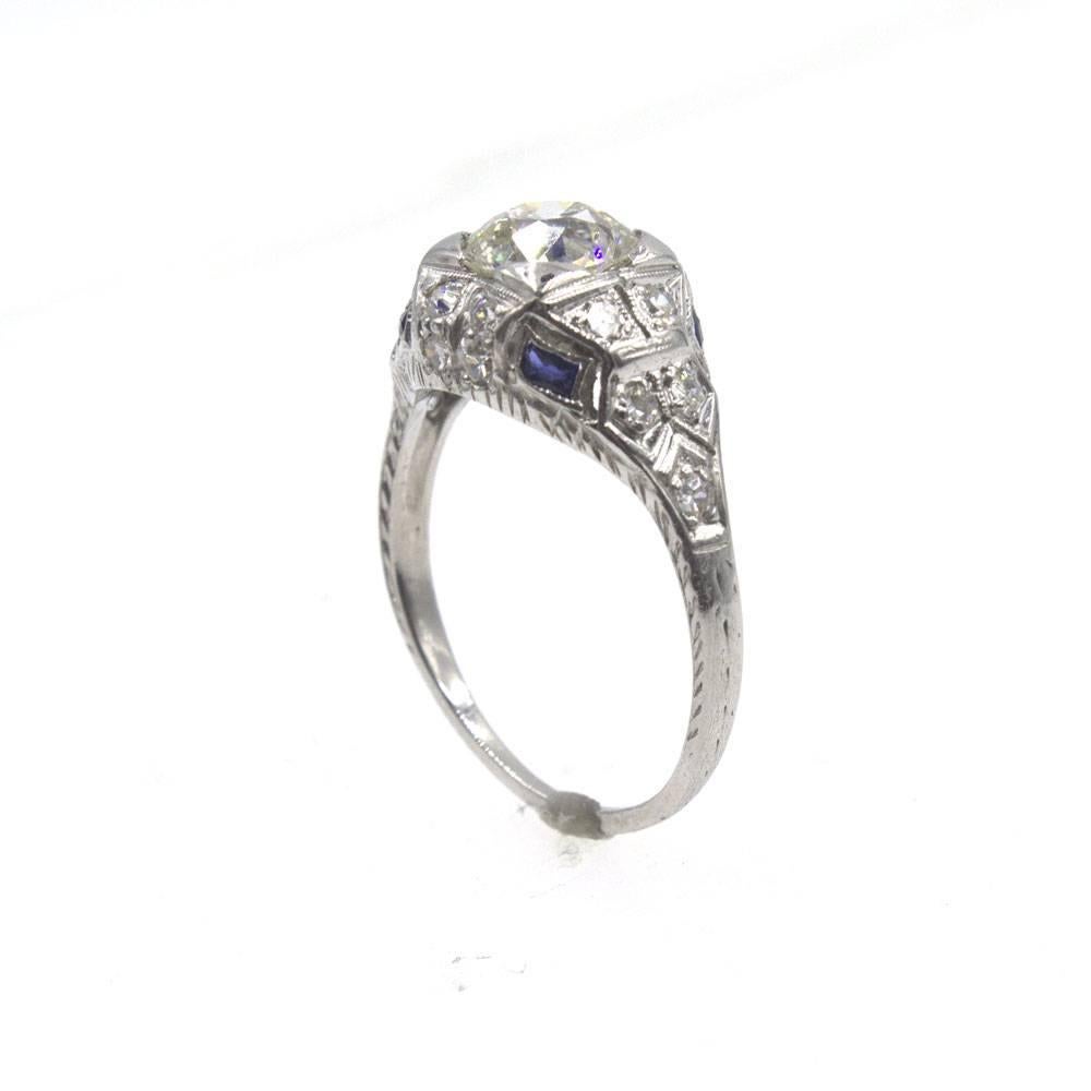 Beautiful Art Deco diamond ring crafted in platinum. The ring is set with an 1.31 carat Old European Cut diamond graded J color and SI2 clarity.  The mounting features diamonds ( approximately .25 ctw) and sapphire accents and measures 10mm in width