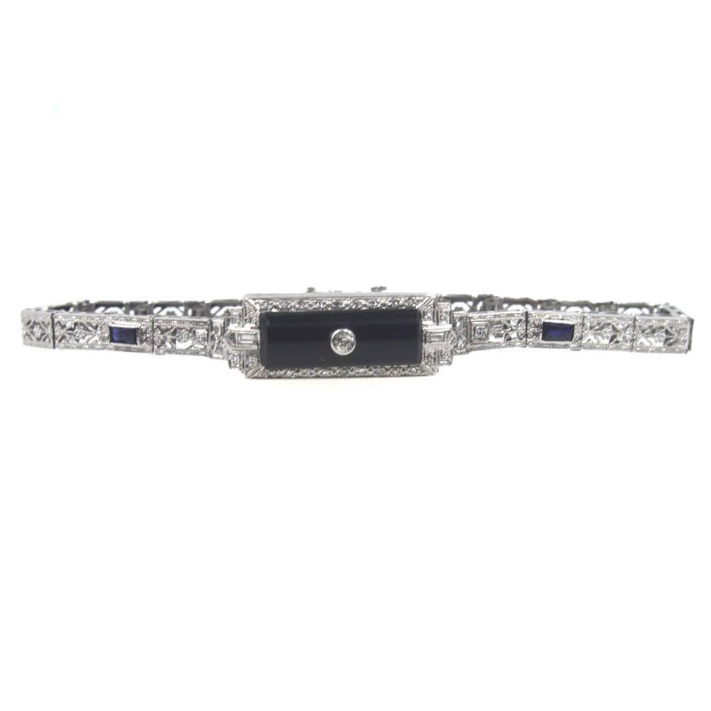 This beautiful platinum filigree bracelet features a rectangular onyx gemstone, diamonds, and accent sapphires. The 33 diamonds equal approximately .50 carat total weight. The bracelet measures 7 inches in length and 10mm in width. 