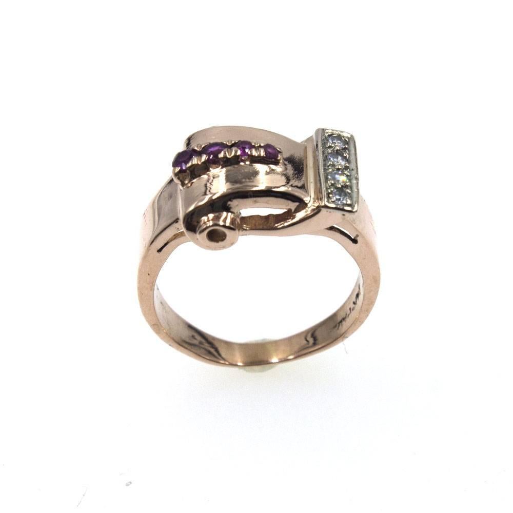 This original Retro diamond and ruby buckle ring is crafted in 14 karat rose gold. The ring features 4 diamonds, that equal approximately .10 carat total weight, and 4 rubies. The ring is currently size 6.5 (can be sized) and measures 12mm in width. 