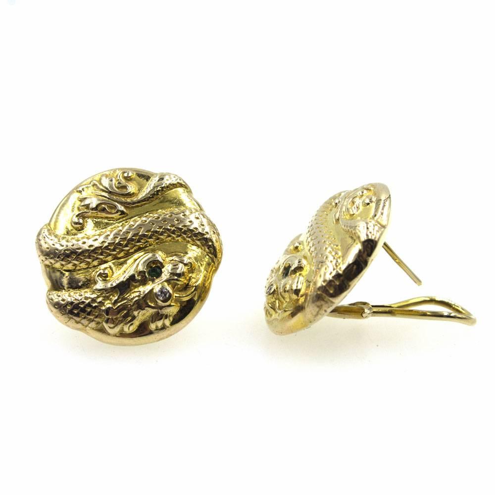 Beautifully crafted 14 karat yellow gold earrings feature a single diamond and emerald accent. The textured snake design adds style to the round earrings. The earrings have omega backs and measure 1 inch in diameter. 