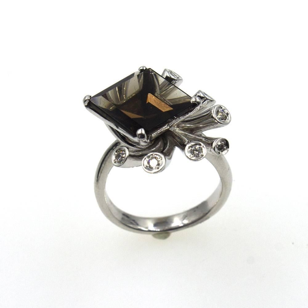 This amazing cocktail ring features a 6.15 carat square cut smoky topaz surrounded by bursts of diamonds. Crafted in 18 karat white gold, this contemporary style ring measures approximately 1.0 inch in width and 1.0 inch in length. Currently size