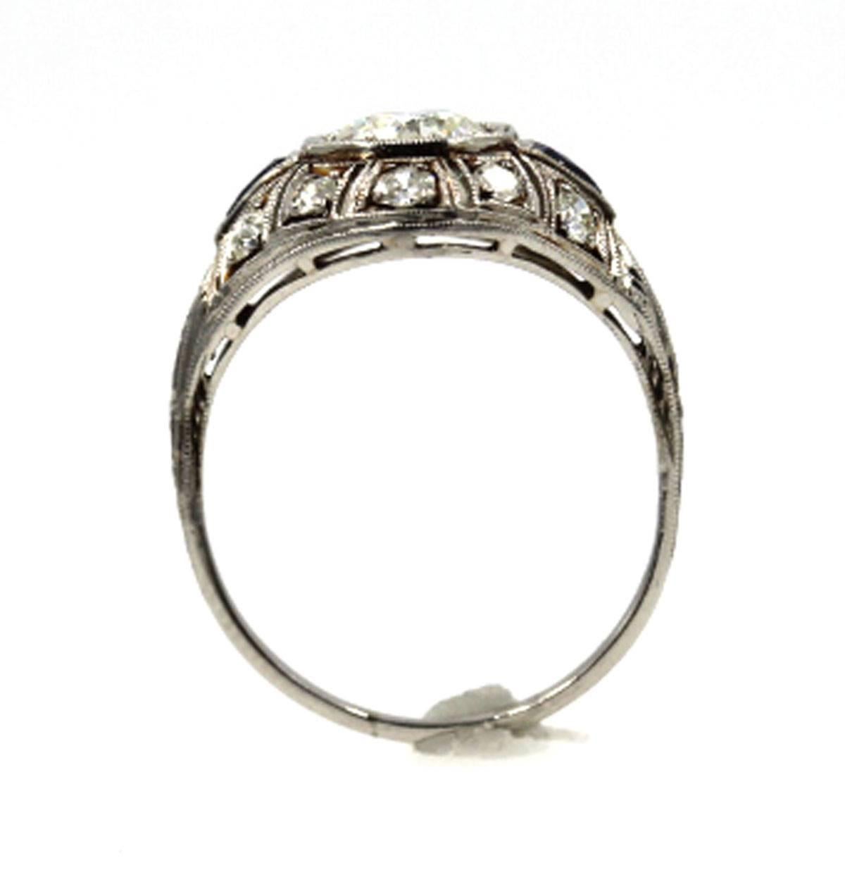 This original Art Deco ring features a 1.07 carat round Old European Cut center diamond graded J color and SI1 clarity. There are approximately 10 side diamonds equaling 1/2 cttw, and 2 accent sapphires around the center. The ring is .5 inches from