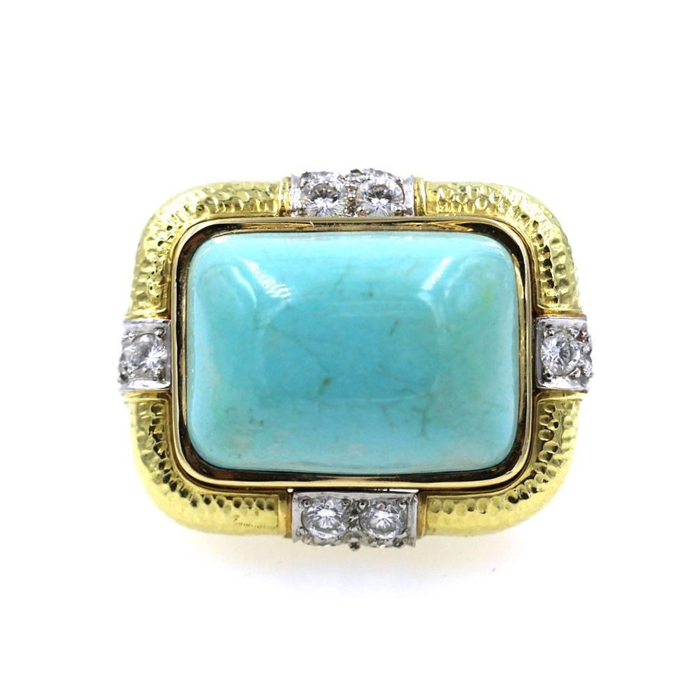 This fabulous ring by David Webb features a rectangular cabochon turquoise gemstone that is set east to west in textured 18 karat yellow gold. There are 12 surrounding round brilliant cut diamonds that equal approximately 1.20 carat total weight.