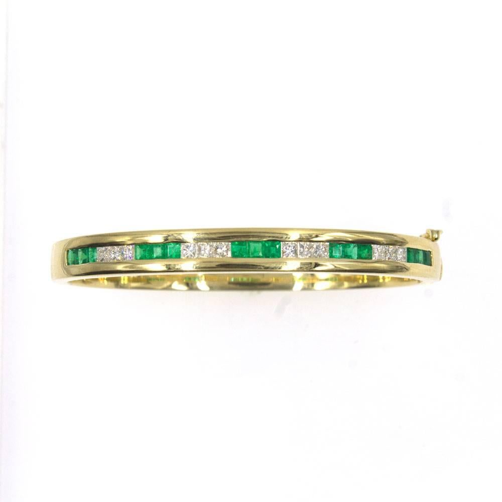 This beautiful  diamond  emerald bangle bracelet by Tiffany & Co. is crafted in solid 18 karat yellow gold. The bangle features alternating brilliant princess cut diamonds and bright green emeralds. There are approximately 1.25 carat total