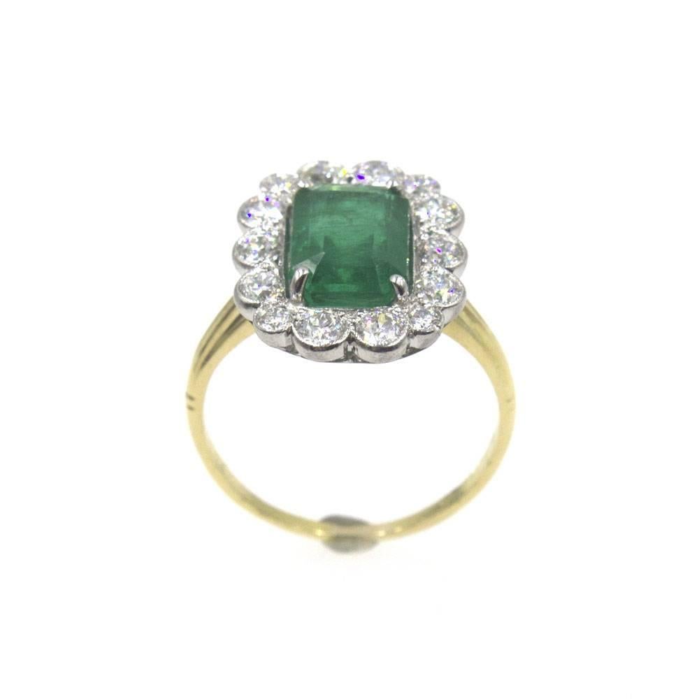 Designed with platinum and 18 karat yellow gold, this beautiful emerald and diamond ring is circa 1930's. The bright green emerald weighs approximately 3.07 carats and is surrounded by 14 Old European Cut diamonds. The diamonds are graded G-H color,