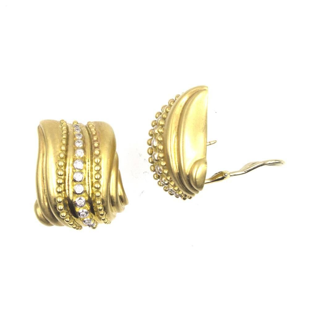 These luxurious diamond textured earrings are fashioned in satin finished 18 karat yellow gold. Twenty four round brilliant cut diamonds are set down the middle as well as studded textured yellow gold. The earrings measure 1.0 inch in length and .75