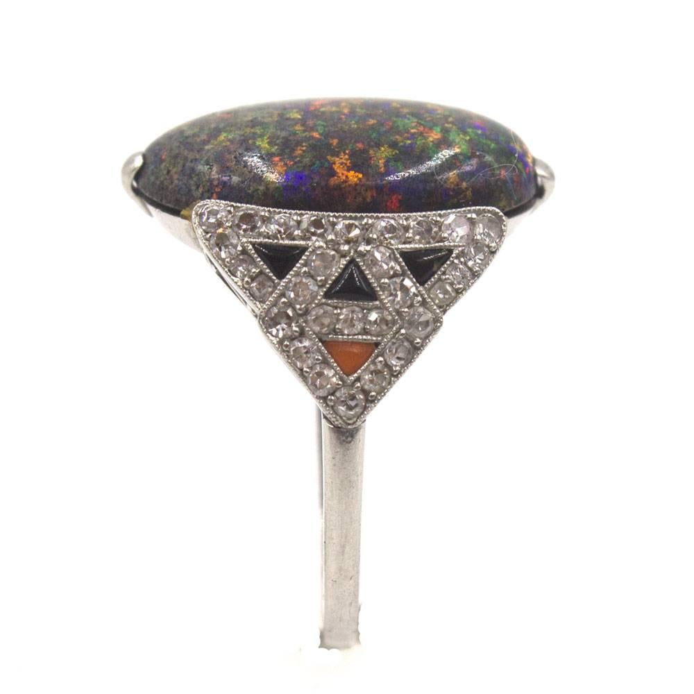 This magnificant Art Deco ring features a black opal set in a diamond onyx and coral accented platinum mounting. The colorful black opal measures 13 x 18mm. The platinum mounting features .50 carat total weight of diamonds and is currently size 7