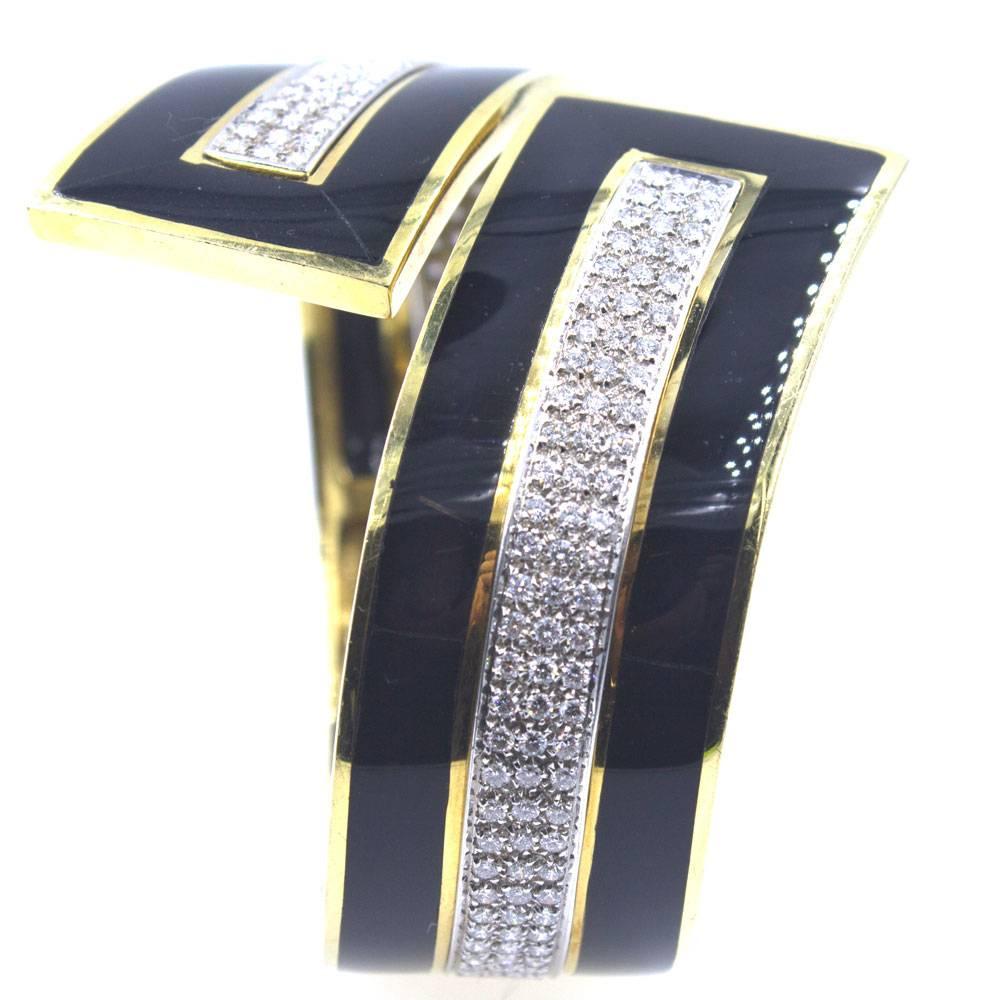Make a statement with this fabulous retro style diamond and onyx bracelet. The large bypass bangle features 4 carats of round brilliant cut diamonds set in rectangular sections surrounded by onyx and 18 karat yellow gold. The hinged bangle measures