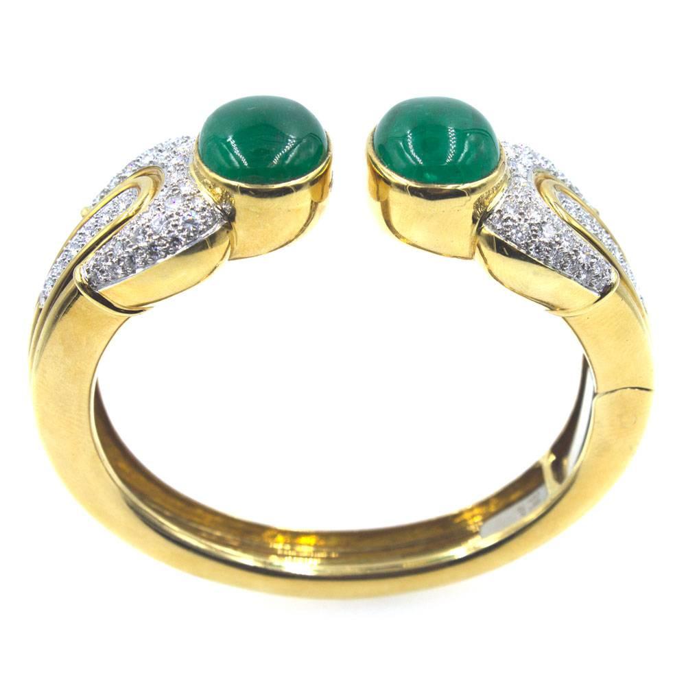 This fabulous 1970's cuff features two large cabochon emerald end caps. The emeralds weigh approximately 25 carat total weight. The hinged cuff is also crafted with textured 18 karat yellow gold and 124 round brilliant cut diamonds. The diamonds