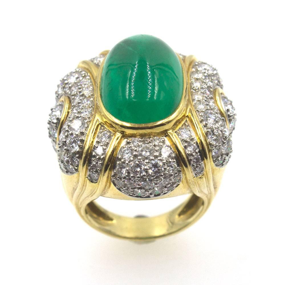 This impressive cabochon emerald and diamond ring is fashioned in 18 karat yellow gold and platinum. The emerald is approximately 13.85 carats and is surrounded by 116 round brilliant cut diamonds. There are approximately 4.00 carat total weight of