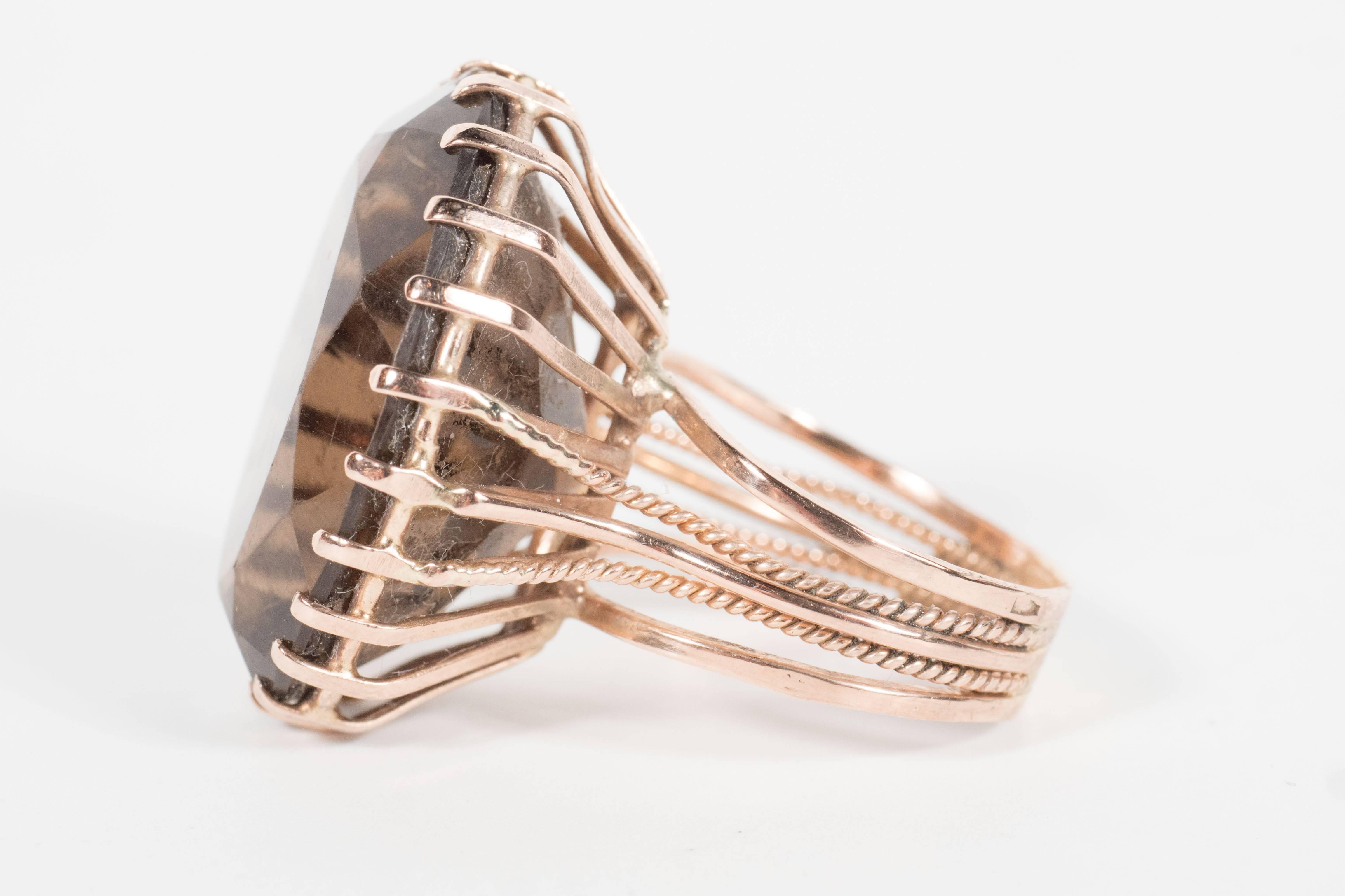 This stunning large oval cut smoky topaz has been securely fitted in a multi prong 14kt yellow gold setting. Two of the supports have been decorated with a braided design that continues onto the band of the ring. With its elegant sable hued topaz