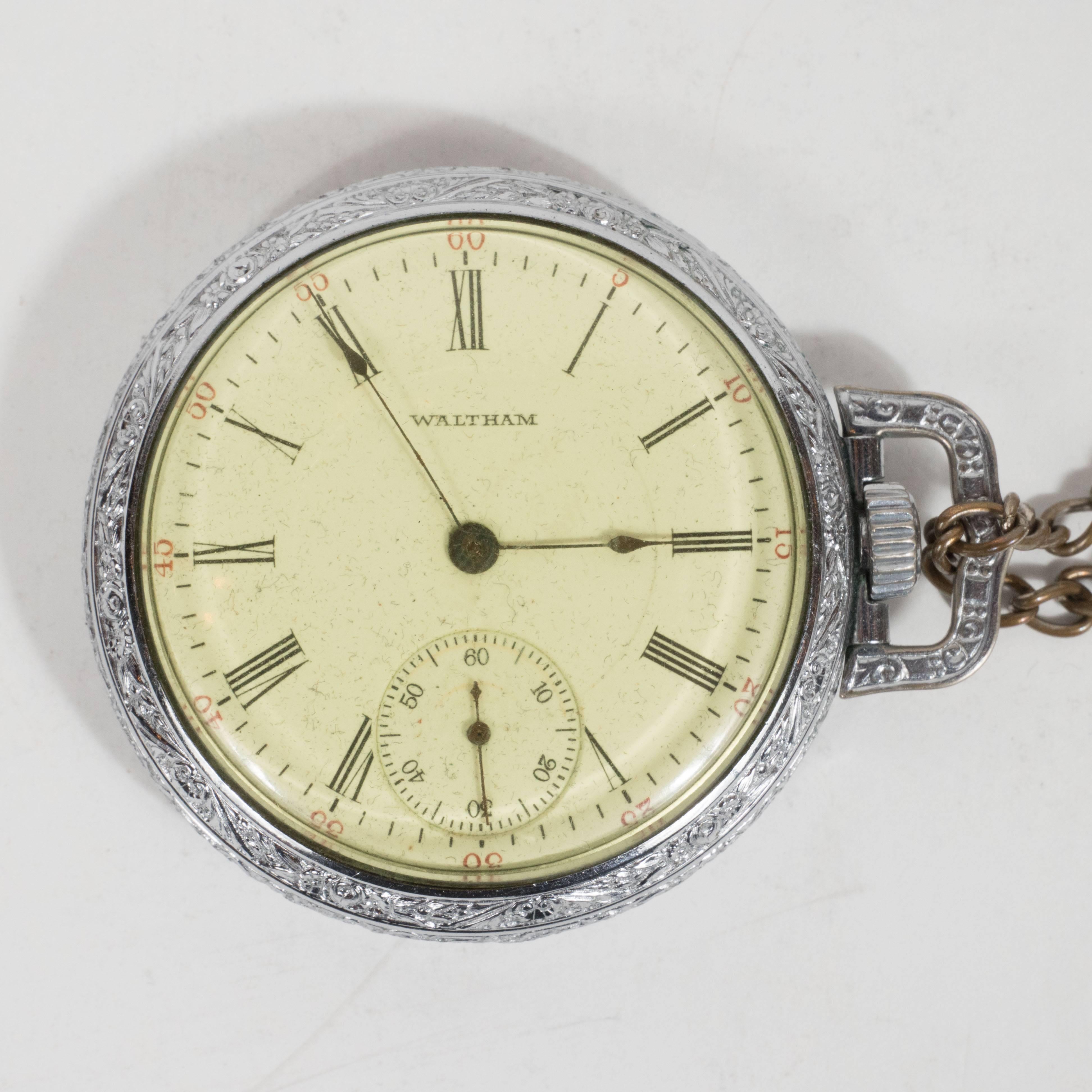 This classic chronometer pocket watch features delicate reed shaped hour and minutes hands on the main dial, roman numerals, and an hour maker circumscribing the perimeter of the face in a ruby red Art Deco font. "Waltham," the