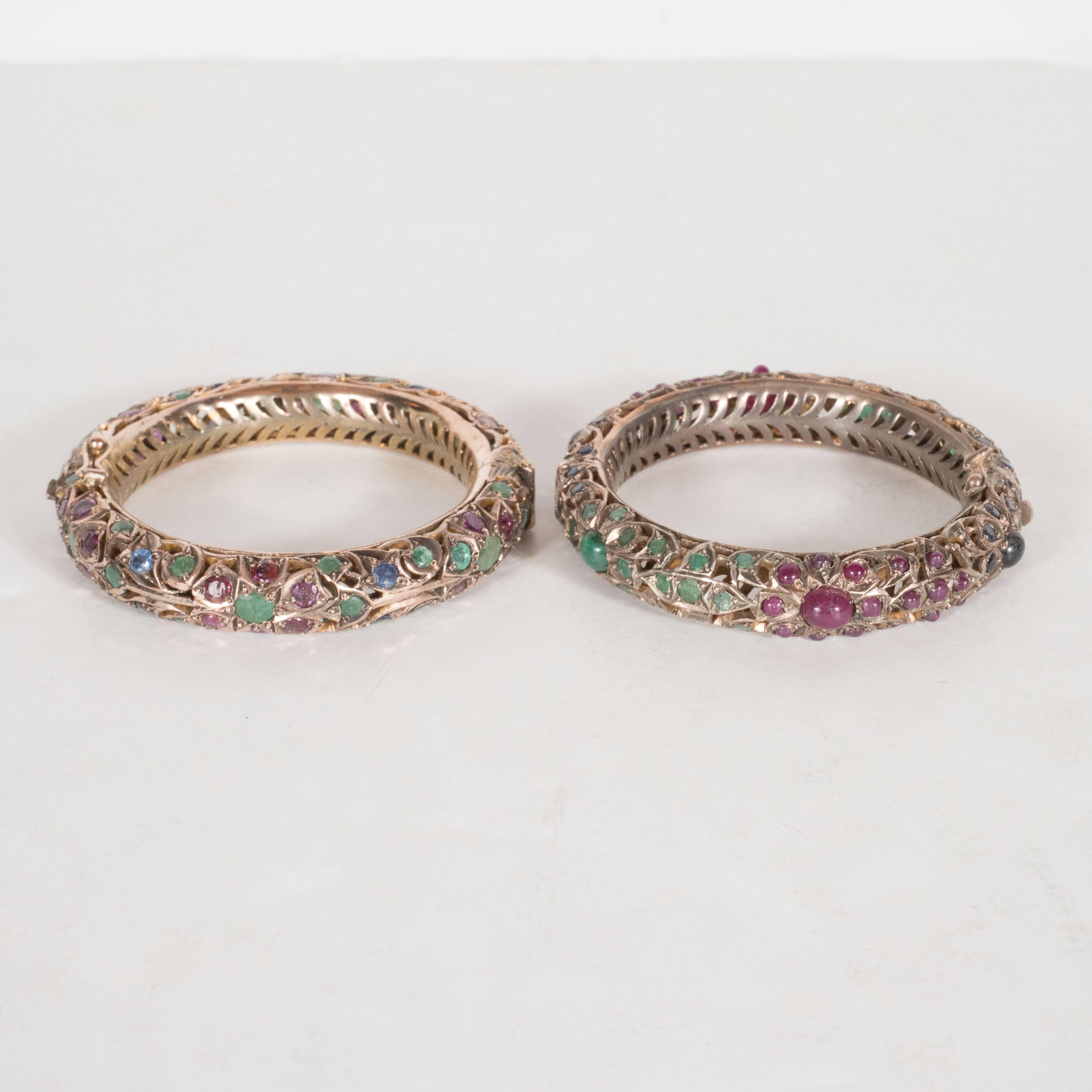 This Exquisite pair of bangle bracelets features round cut sapphires, rubies and emeralds set in 12 karat white gold. It exhibits Moorish geometric designs throughout. The inside is perforated with horizontally configured half crescents. It includes